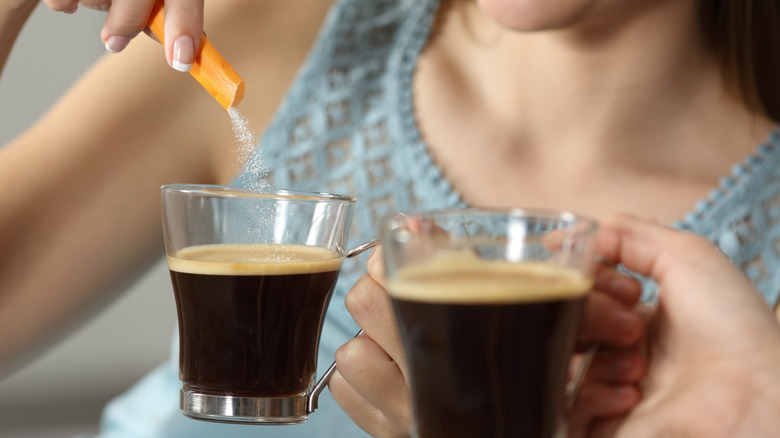 woman pouring sugar sweetener into coffee