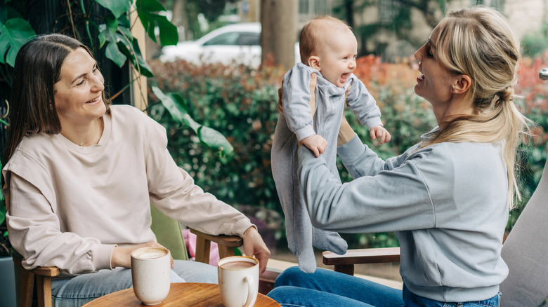 Two women catch up over coffee, one holding a baby