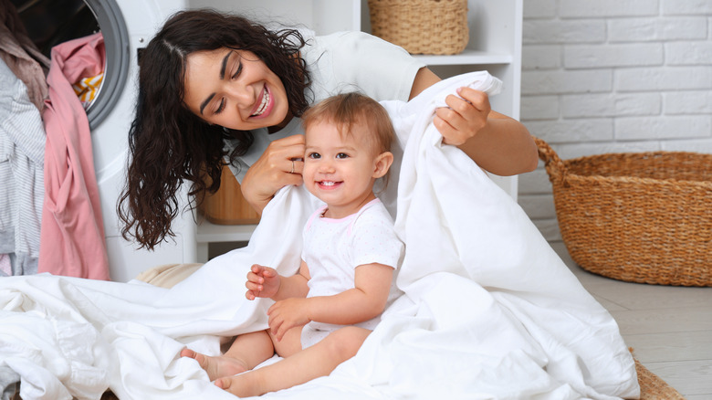 Mom smiles as she wraps baby in a clean towel while they do laundry together