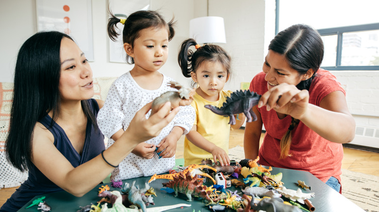 Two mothers with young daughters playing with dinosaurs