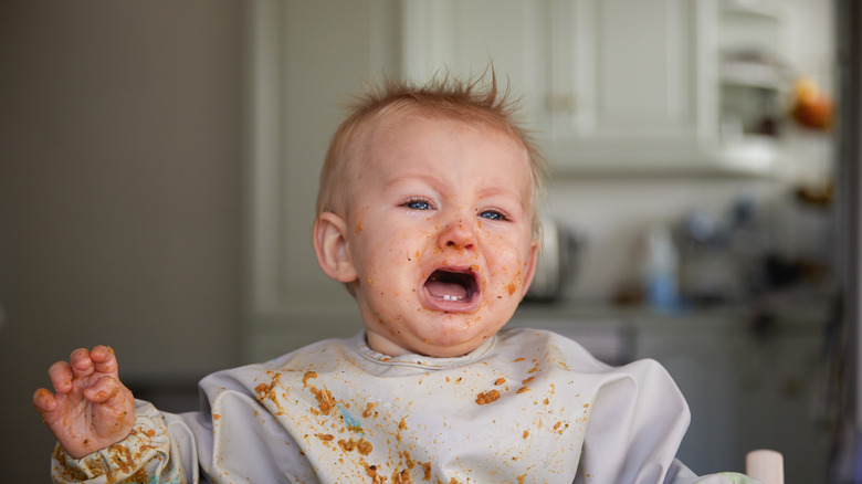 baby boy with food on face screaming in high chair