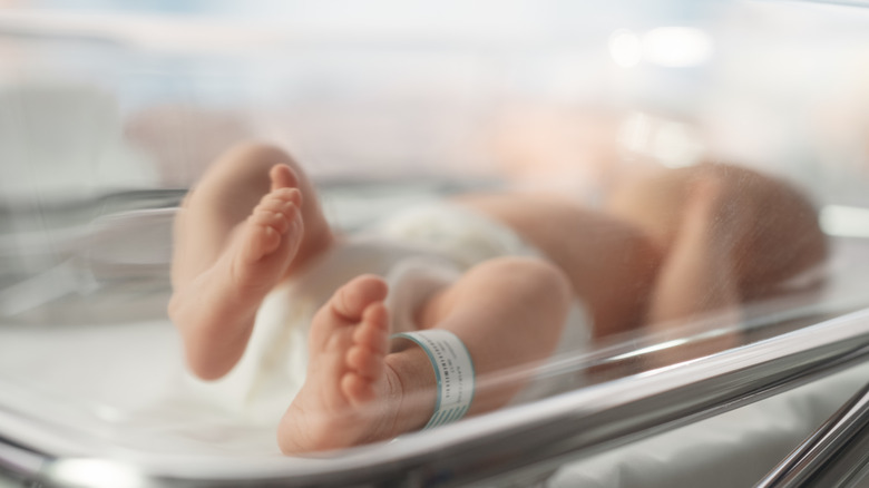 a newborn baby lies in a hospital crib