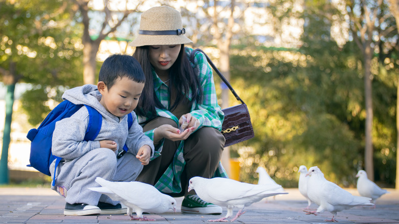 mom and young child kneeling and feeding birds