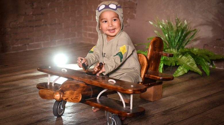 baby dressed like a pilot and sitting in a toy airplane