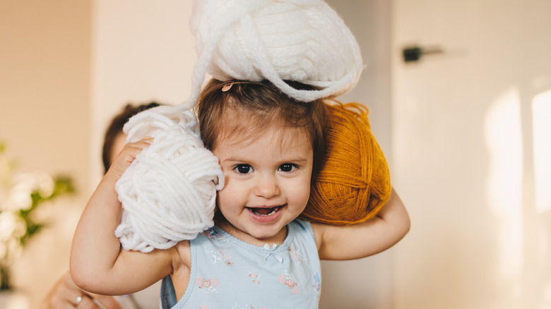 toddler holding balls of yarn on her shoulders and head