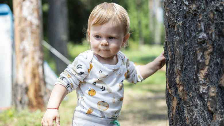 toddler touching a tree trunk and looking thoughtful