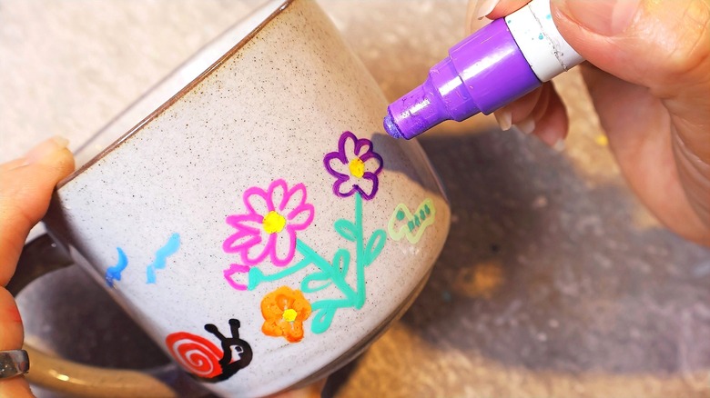 Close-up of a hand painting flowers onto a speckled ceramic mug with paint markers