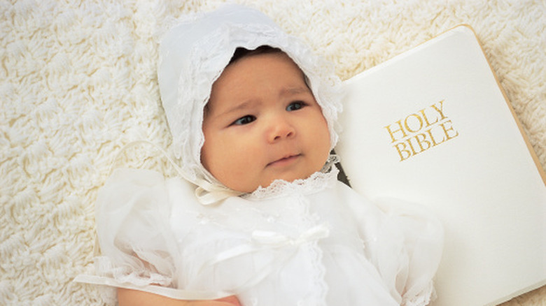 baby in a white outfit next to a Bible