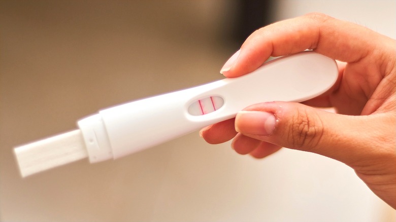 Hand holding a positive at-home pregnancy test with two pink lines