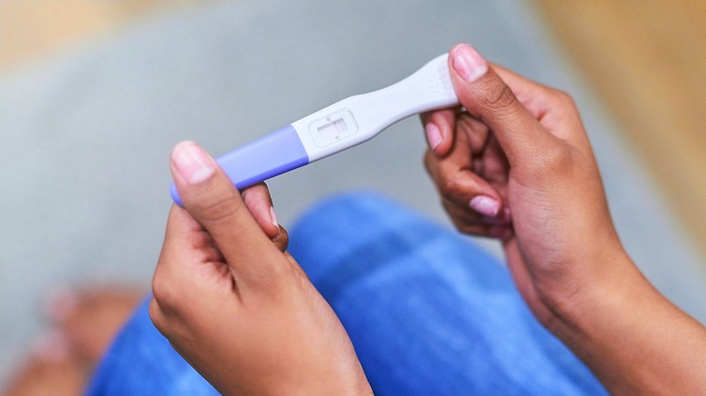 A woman's hands holding a pregnancy test with a purple cap