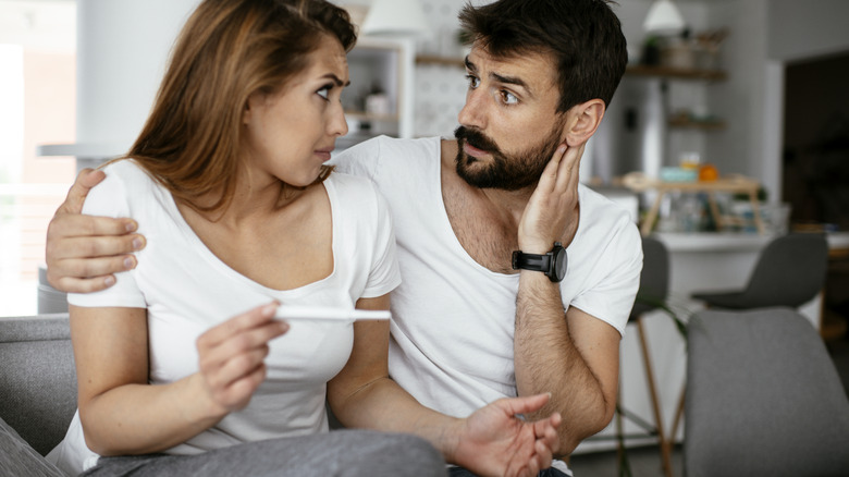 couple sitting and looking confused at the pregnancy test she holds