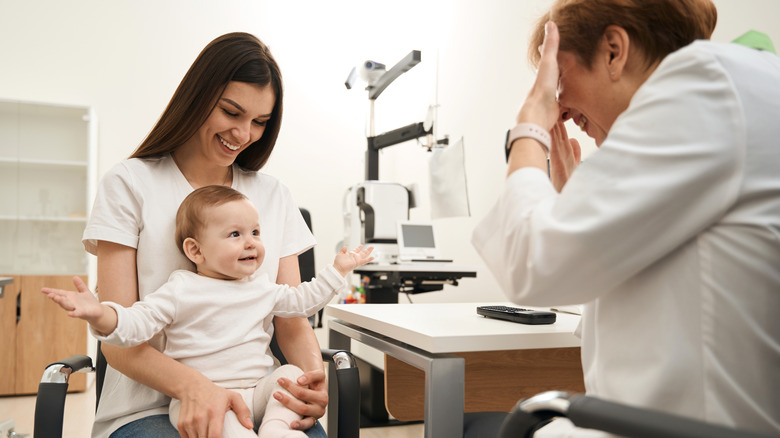 A mother holds a baby who is interacting with a pediatric eye doctor