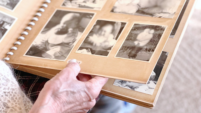 The hand of an elderly person holds a page of an old photo album with photos of family members