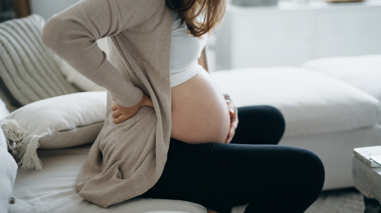 A pregnant woman holds her back and belly while experiencing labor pains