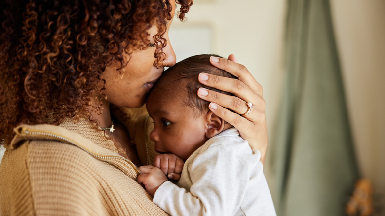 A woman leans in and kisses the forehead of a newborn baby