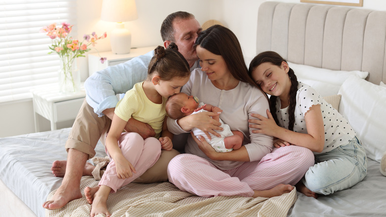 A mother sitting on a bed holding a newborn baby surrounded by a man and two older children