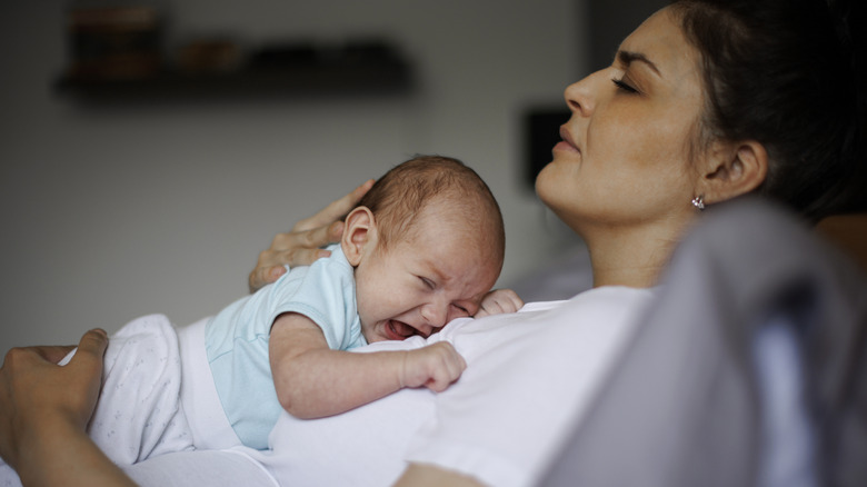Tired-looking mother with crying baby on her stomach