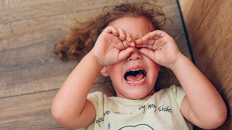 child lying on the floor, upset, with their hands over their eyes