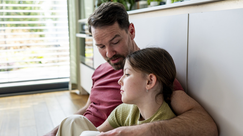 Father and daughter sit together talking with his arm around her