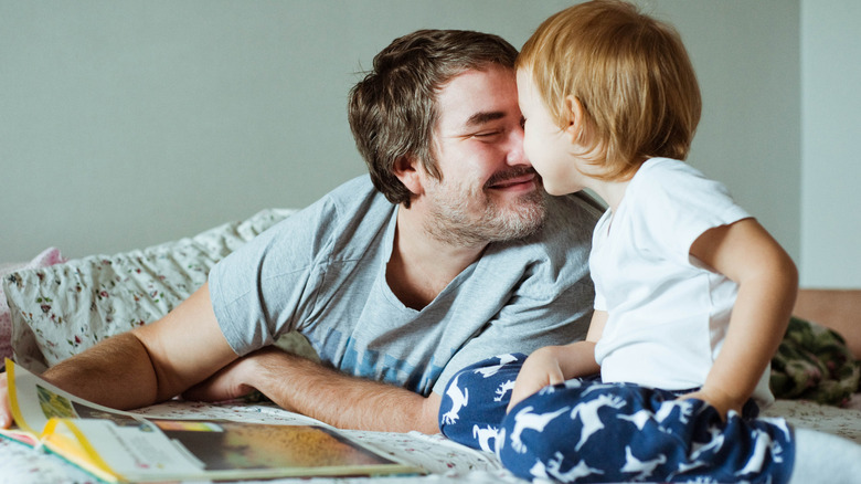 A father nuzzling his child while reading a book before bed
