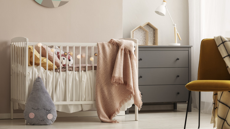 A nursery room with a chair, a dresser, a crib, several stuffed animals, and blankets