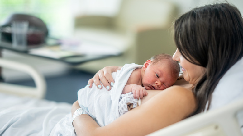Woman smiling and holding a newborn baby on her chest in a hospital