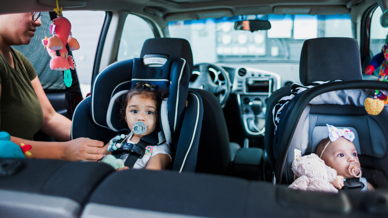 older kid sitting in convertible car seat next to infant in a infant car seat, both rear facing