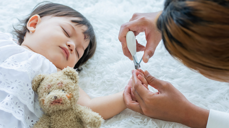 parent clipping baby's nails while they sleep