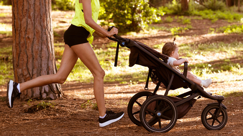 woman running in the forest with a three-wheeled jogging stroller