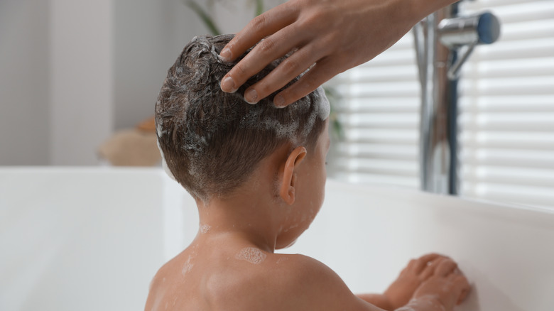 Hands reaching down touching a baby's scalp with water and shampoo